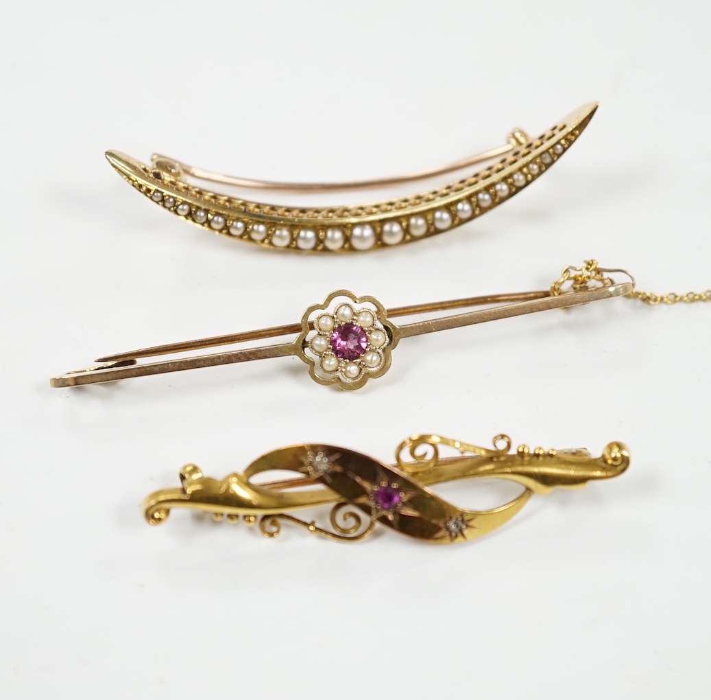 An Edwardian 15ct, ruby and diamond chip set three stone bar brooch, 45mm, a 9ct and gem set bar brooch and a yellow metal and seed pearl set crescent brooch.